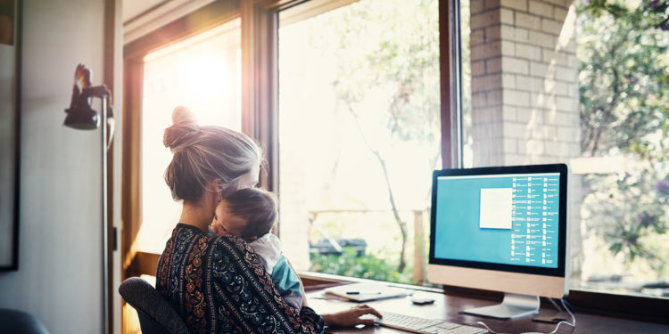 Shot of a young woman working at home while holding her newborn baby son.